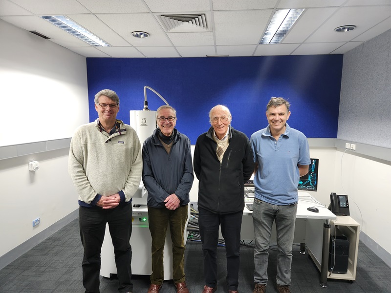 Four men standing in front of a piece of mineral characterisation equipment