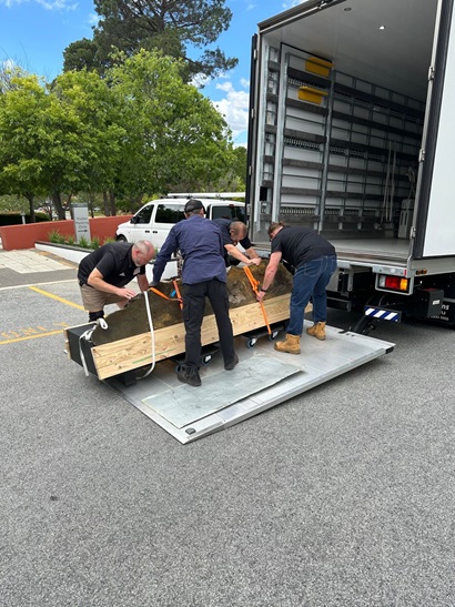 A large chimney like structure being loaded onto a truck by four people. 