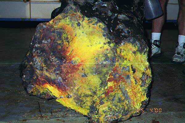 Close-up of the end of the Bikpela chimney, showing vivid orange and yellow hues surrounded by dark, textured surfaces, with a hammer resting on top for scale.