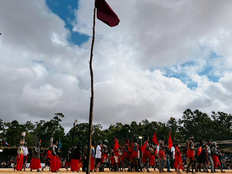 a group of dancers wearing red surround a red flag on a large flag pole