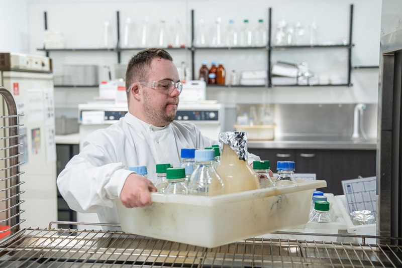 Person in a lab coat carrying a tray of glassware in the lab.