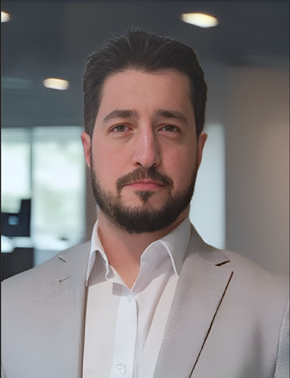 Vinnie wears a pale grey suit and white shirt. We just see from his shoulders up. Vinnie has a beard and moustache. This is a formal corporate photo