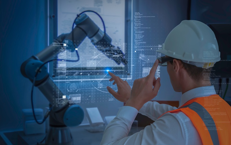 A person wearing a hardhat uses augmented reality and analytics to program a robotic arm 