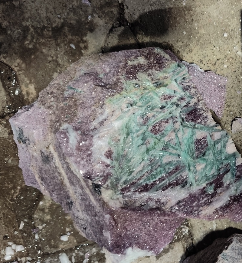 a section of rock, still in the ground, with neon coloured blue-green crystals zig zagging across the rock.
