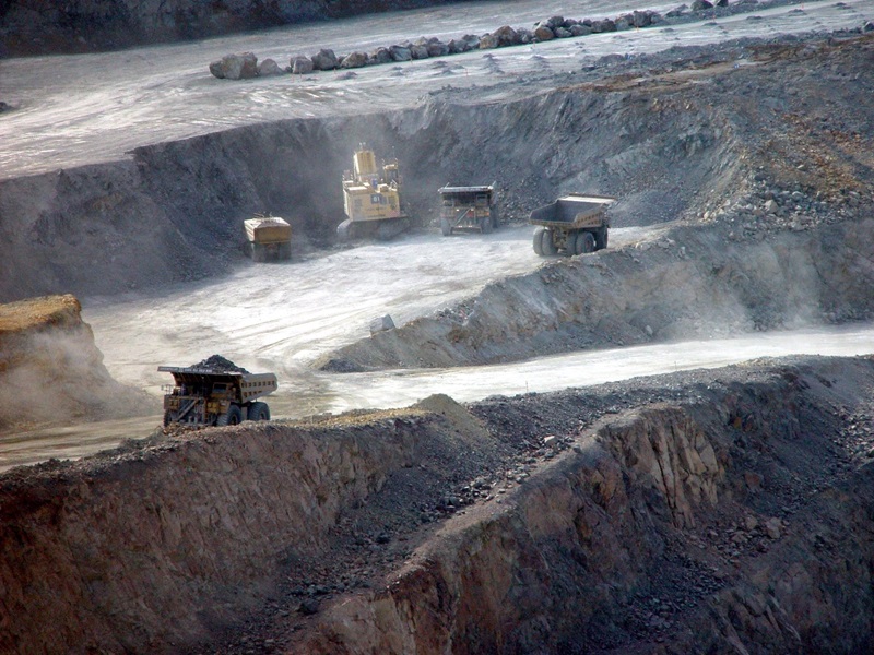 A vast open cut mine with a mix of dump trucks and diggers at various levels on the mine paths