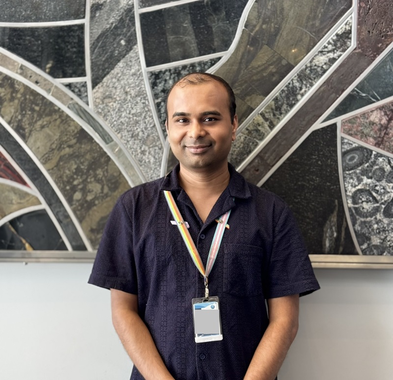 Chirantan stands in front of an abstract painting. He wears a blue polo shirt and smiles at the camera.