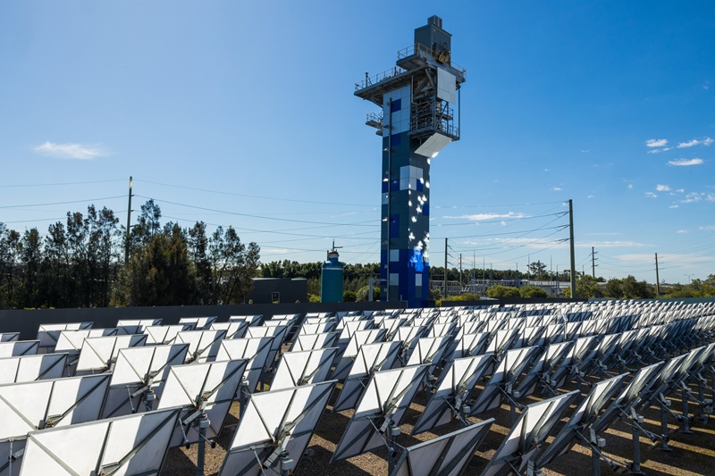 CSIRO heliostat tower and field of solar panels in front of a blue sky.