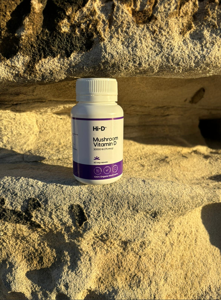 A white plastic container positioned on a rocky surface with a label containing the words Hi-D Mushroom Vitamin D 3000 IU (75 mcg) 60 veg capsules 100% organic mushrooms