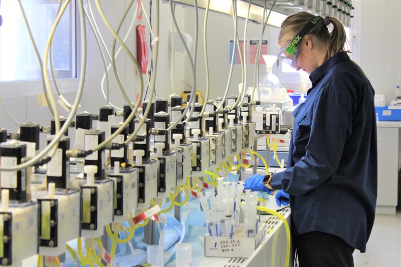 Person in protective glasses and gloves working in a lab at a line of solvent extraction receptacles