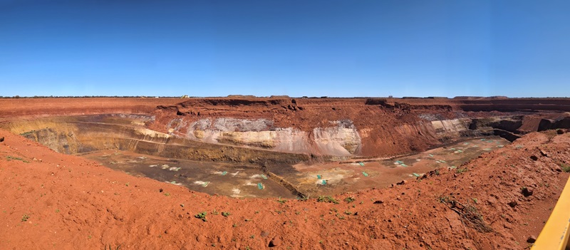 open cut mine with exposed orange earth against a blue sky