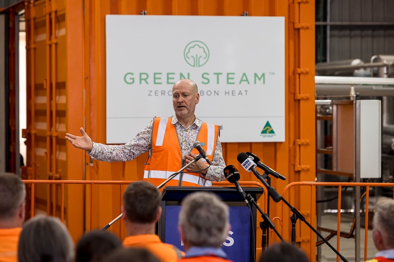 Man presenting in front of Green Steam, on an orange shipping container