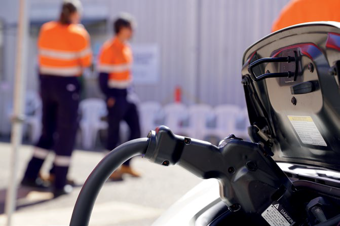 Electric Vehicle with charging cable plugged in with 2 workers in the background.