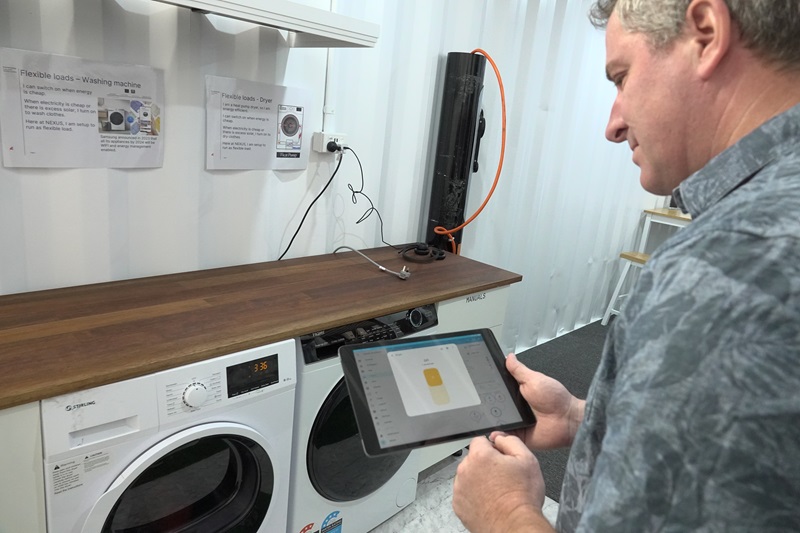 Man holding tablet in front of household appliances including a washing machine and dryer