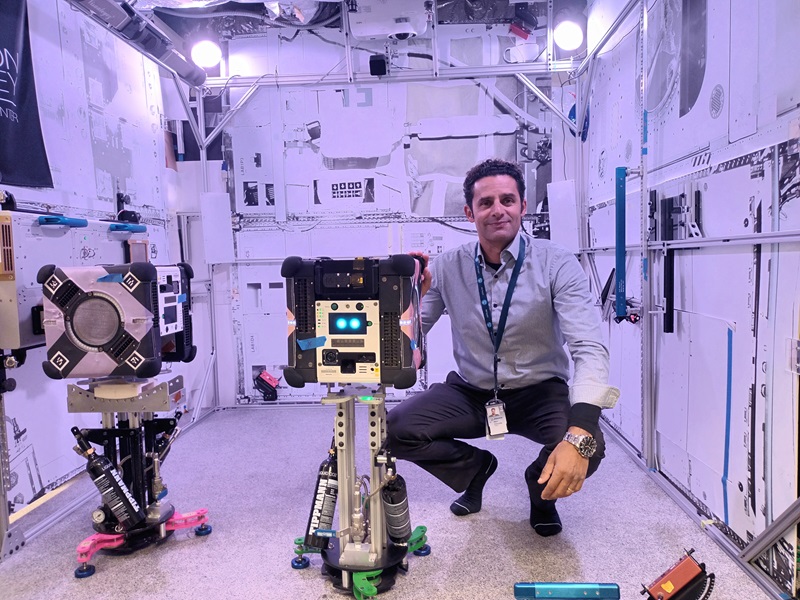 CSIRO researcher Marc Elmouttie squats next to a robot with the rectangular multi-resolution scanner attached in a testing environment to mimic the International Space Station. 