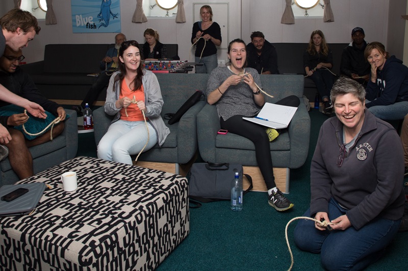 a group of people all laughing and smiling whilst learning to tie knots in a nautical rope