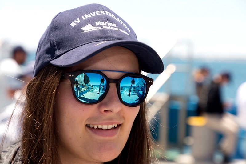 a close up photo of a CAPSTAN student wearing sunglasses and a cap that reads RV Investigator