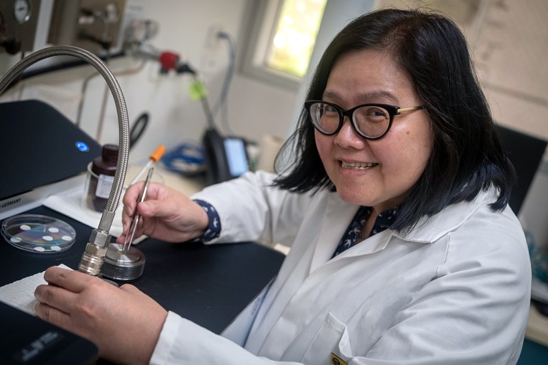 A scientist in a lab coat looks up from her work at the lab bench. 