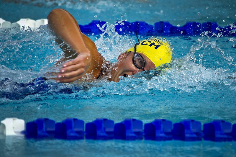 A swimmer wearing a yellow cap and goggles performs the freestyle stroke in a pool