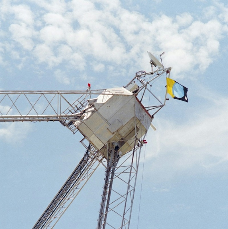 A metal cabin pointing to the sky, with a blue and yellow flag attached to it.