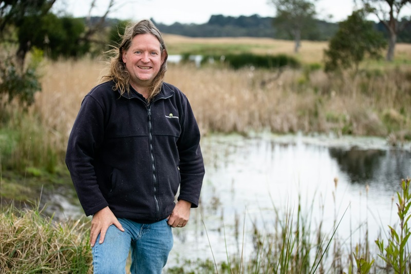 Man standing in front of a 'frog bog' wetland that looks like a farm dam in a natural setting.