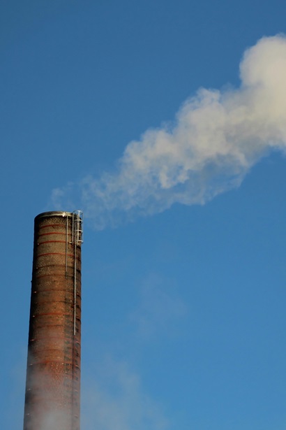 Close up of dense white smoke coming out of an industrial factory chimney against a blue sky background.