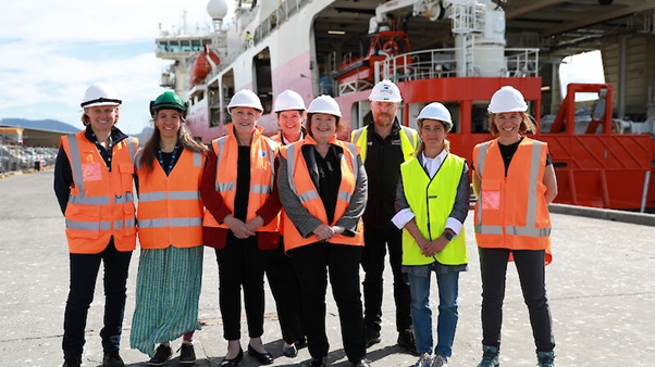 Eight people in fluorescent vests stand in front of a docked vessel.