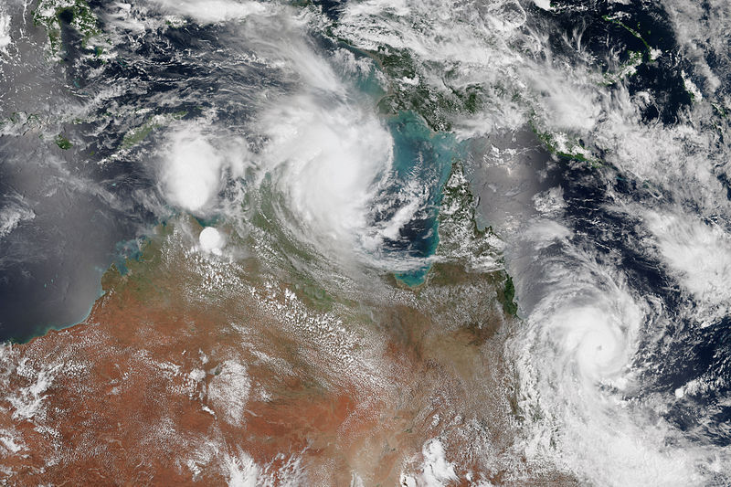 satellite image of two tropical cyclones forming over northern Australia. One cyclone is positioned near the coast of Queensland, while the other is developing over the Northern Territory. The image shows swirling cloud formations over the ocean and land.