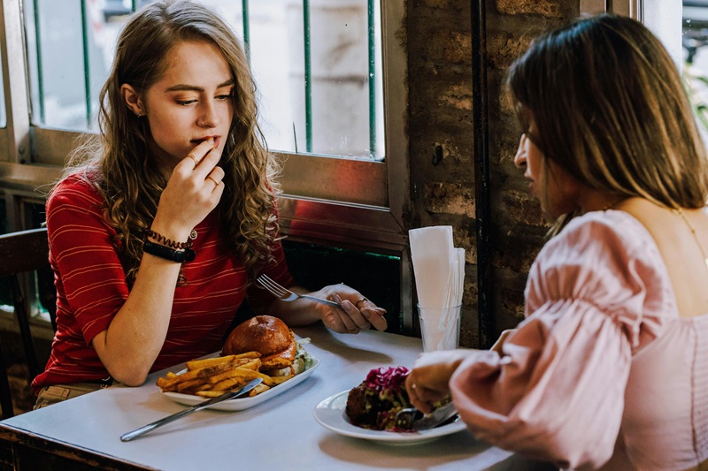 Two women sit at a restaurant eating burgers.