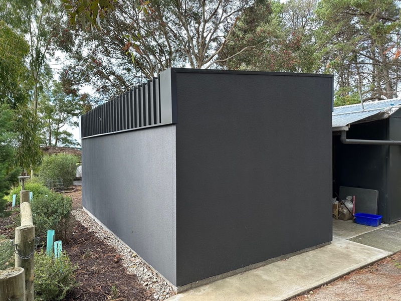 A modern, fire-proof building with dark walls and vertical metal slats, surrounded by trees and vegetation