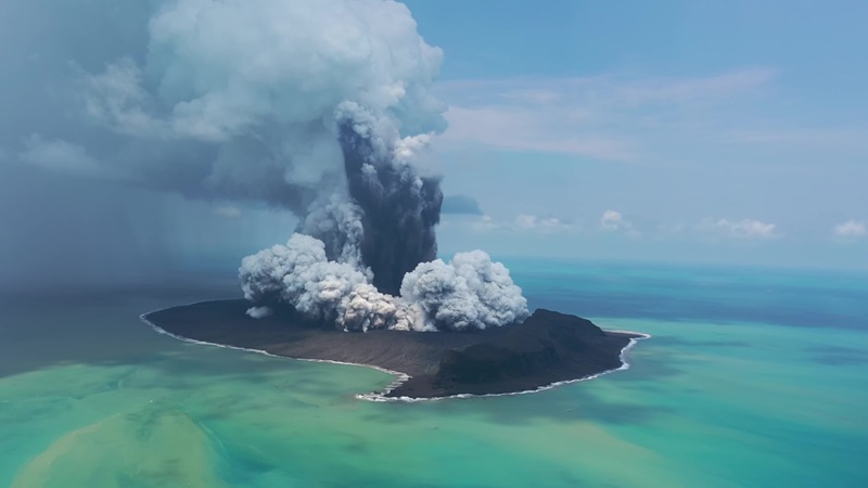 Smoke and ash explode from an island volcano surrounded by blue-green ocean waters,