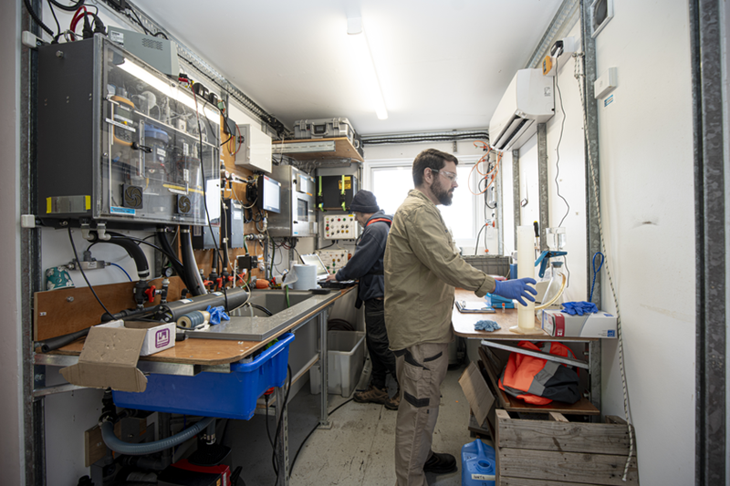 Two scientists in a container laboratory, wearing safety gear. They are analysing water samples.